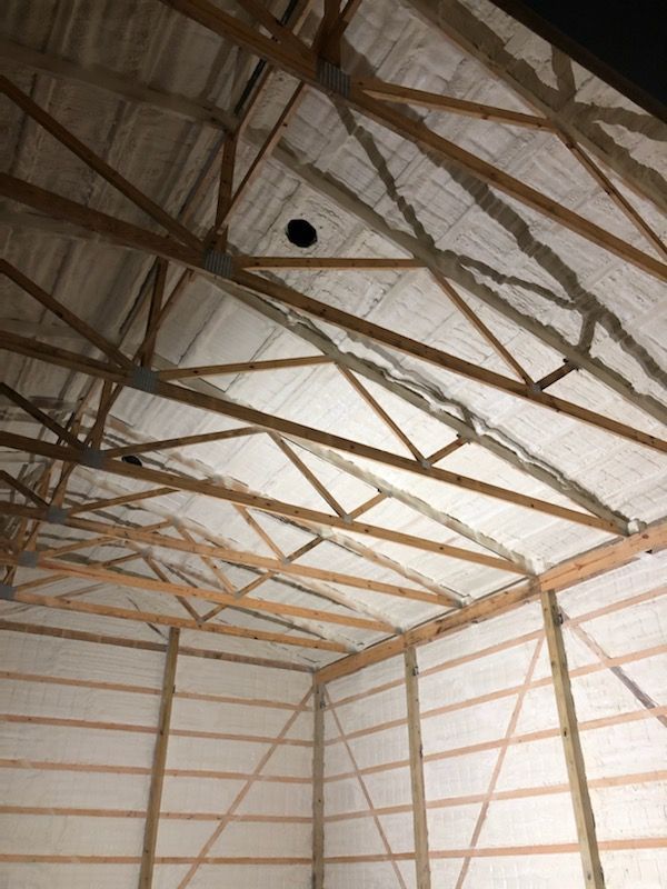 Inside a barn-like room, wooden rafters support a white insulated ceiling and walls.