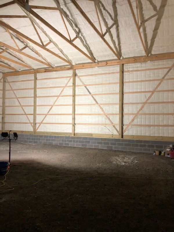 Empty barn interior with wooden trusses, white walls, and a dirt floor
