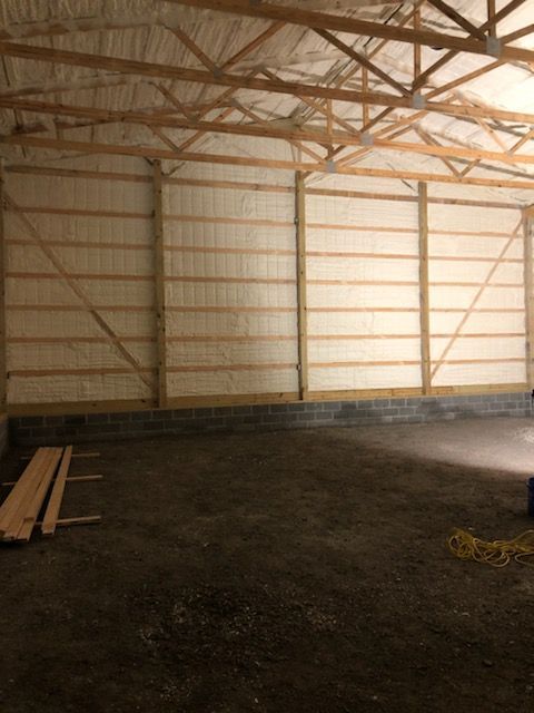 Empty barn interior with wooden trusses, beige walls, and dirt floor.