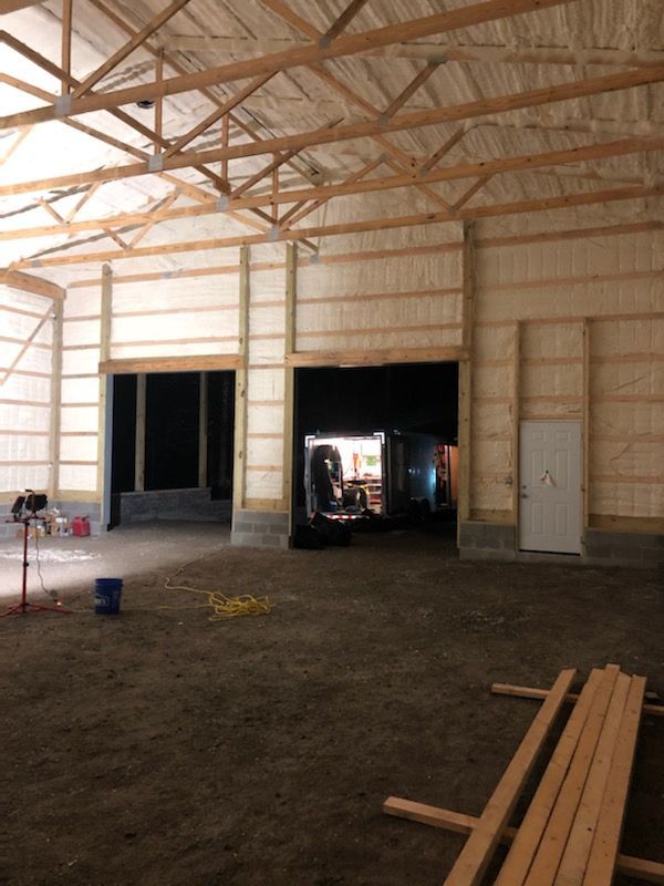 Large unfinished warehouse interior with exposed wood trusses, open doorways, and lumber stacked on the floor.