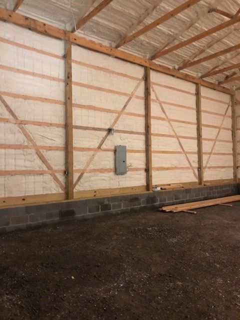 Interior of a wooden barn wall with diagonal braces, concrete block base, and a gravel floor