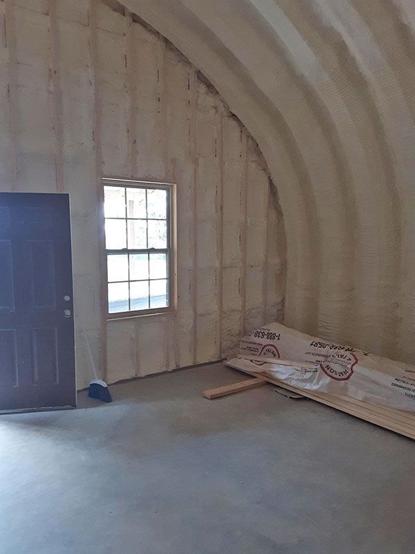 Bare interior room with arched insulated walls, a blue door, a window, and construction materials on the floor