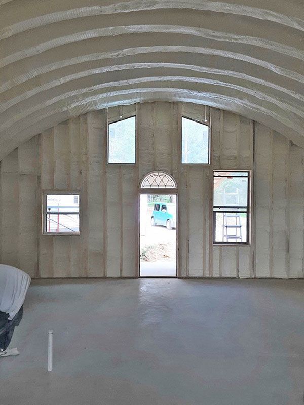 Empty unfinished room with curved ceiling, concrete floor, and open doorway with windows on either side.