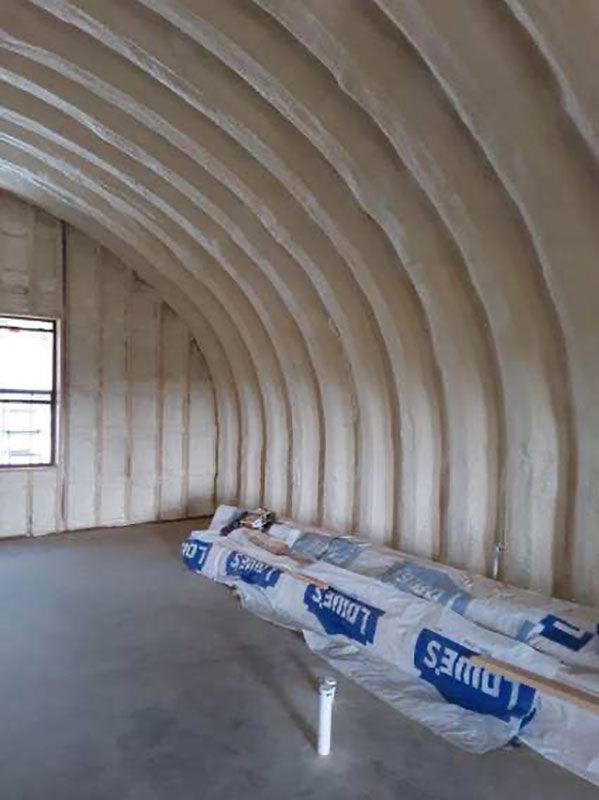 Bare insulated interior with curved ceiling, small window, and stacked construction materials on the floor