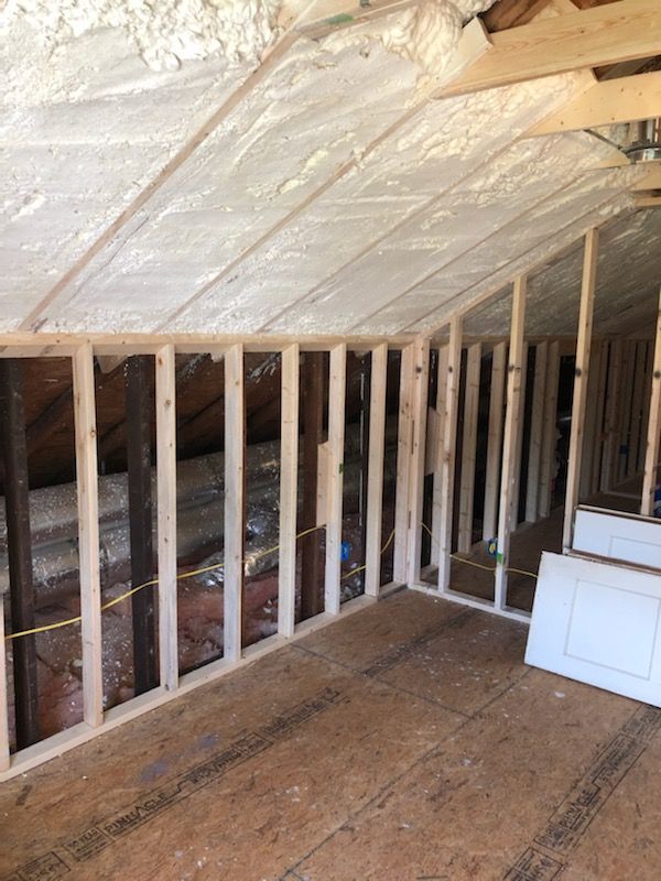 Unfinished attic with exposed wall studs and spray foam insulation on a slanted roof, with a white cabinet.