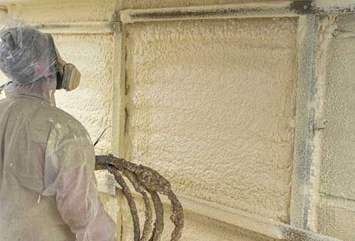 Worker spray-foaming insulation on a wall in a construction setting