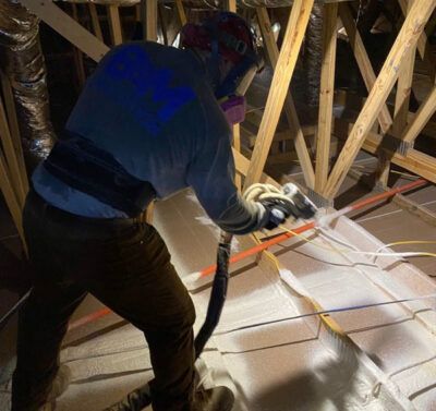 Worker using a circular saw to cut plywood in an attic with exposed wooden rafters