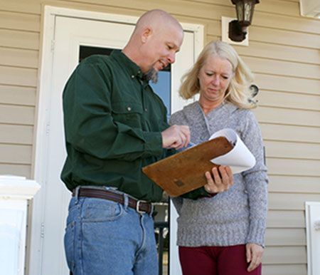 when-to-call-in-the-pros Man in green shirt showing document on clipboard to concerned woman on a porch