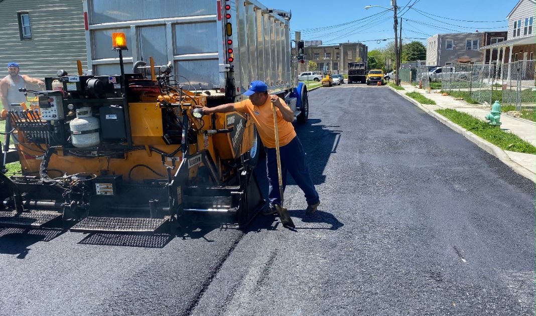 A man is standing next to a machine that is laying asphalt on a street.