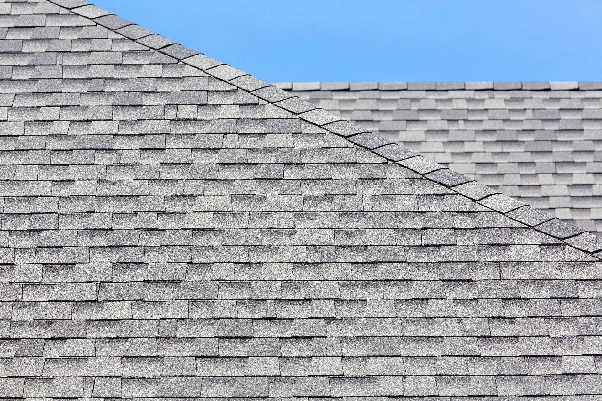 Gray asphalt shingle roof against a clear blue sky.