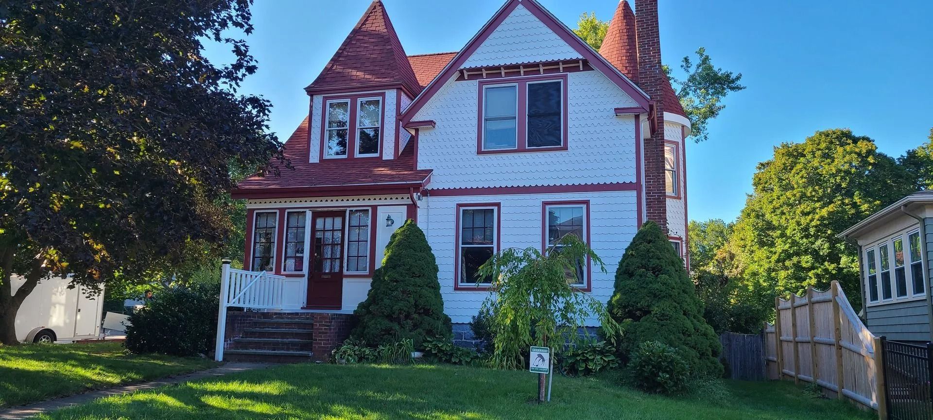 White Victorian house with red roof, two turrets, and porch on a sunny day.