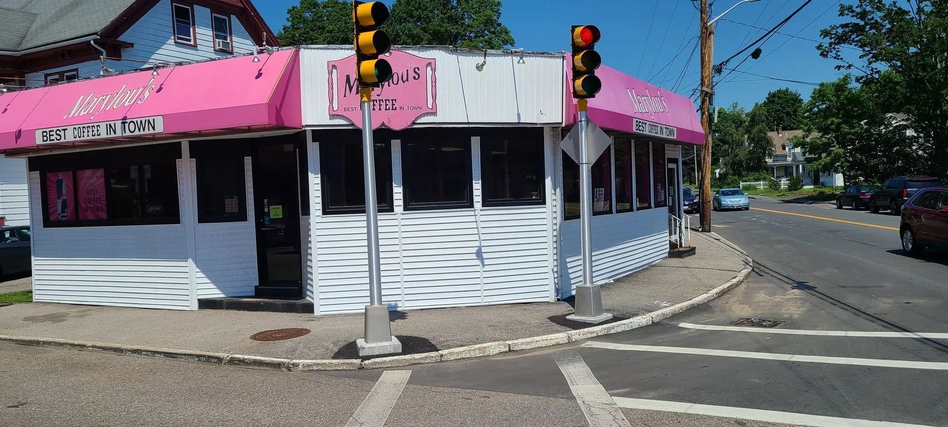 A white building with pink awning. A street corner with traffic lights and a sign for 