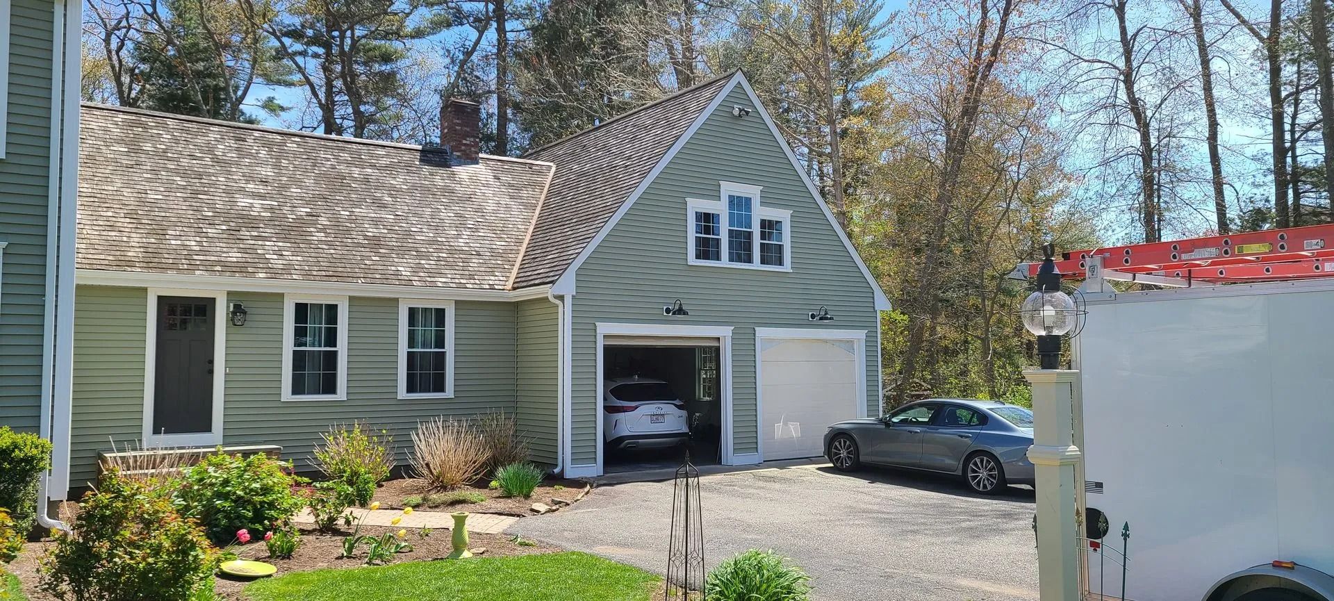 A light green house with a garage, a car parked in the driveway, and another inside the open garage.