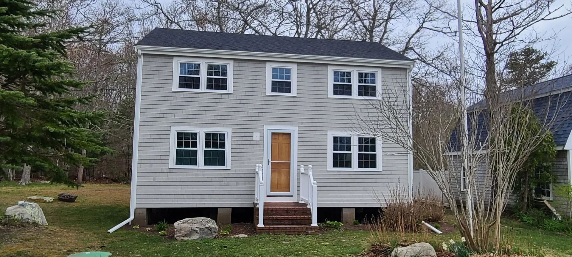 Two-story weathered house with a white front door and surrounding trees.