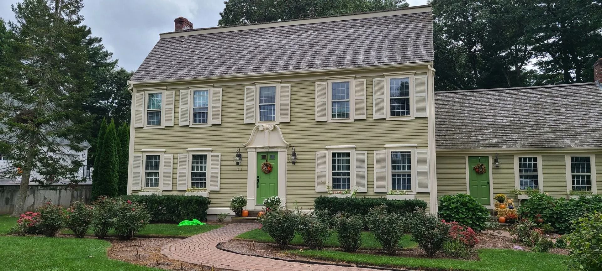 Two-story light green house with white shutters, green door, and stone walkway.