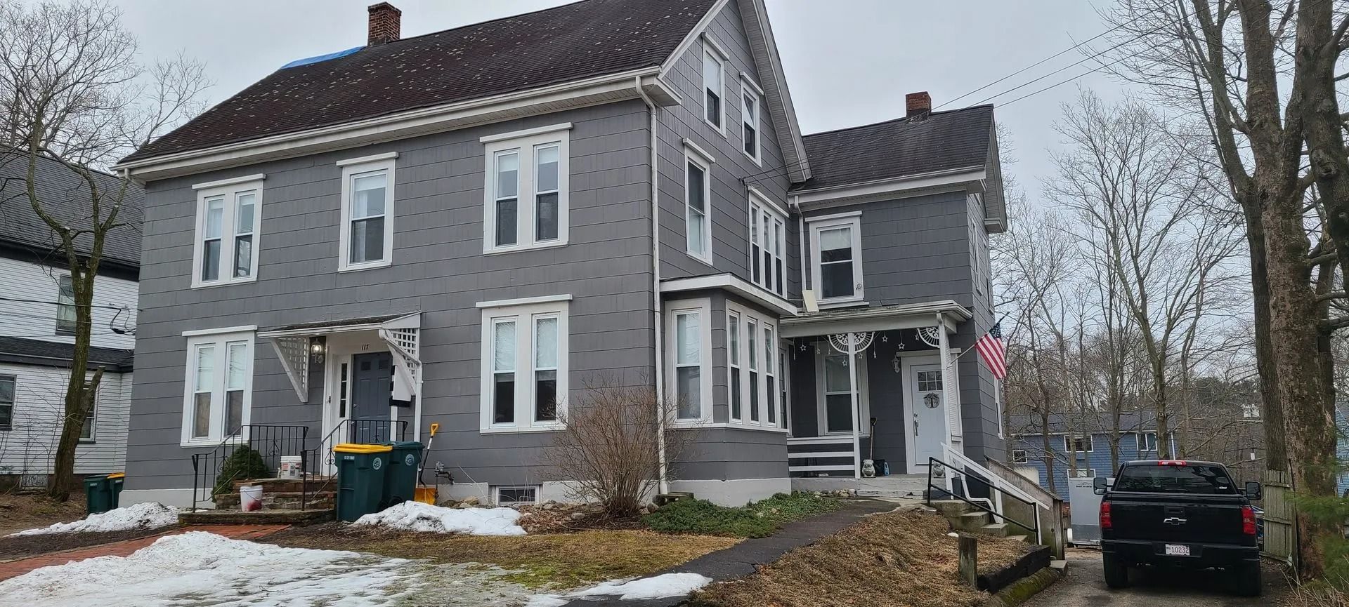 Gray multi-story house with many windows and an American flag. Snow on ground.
