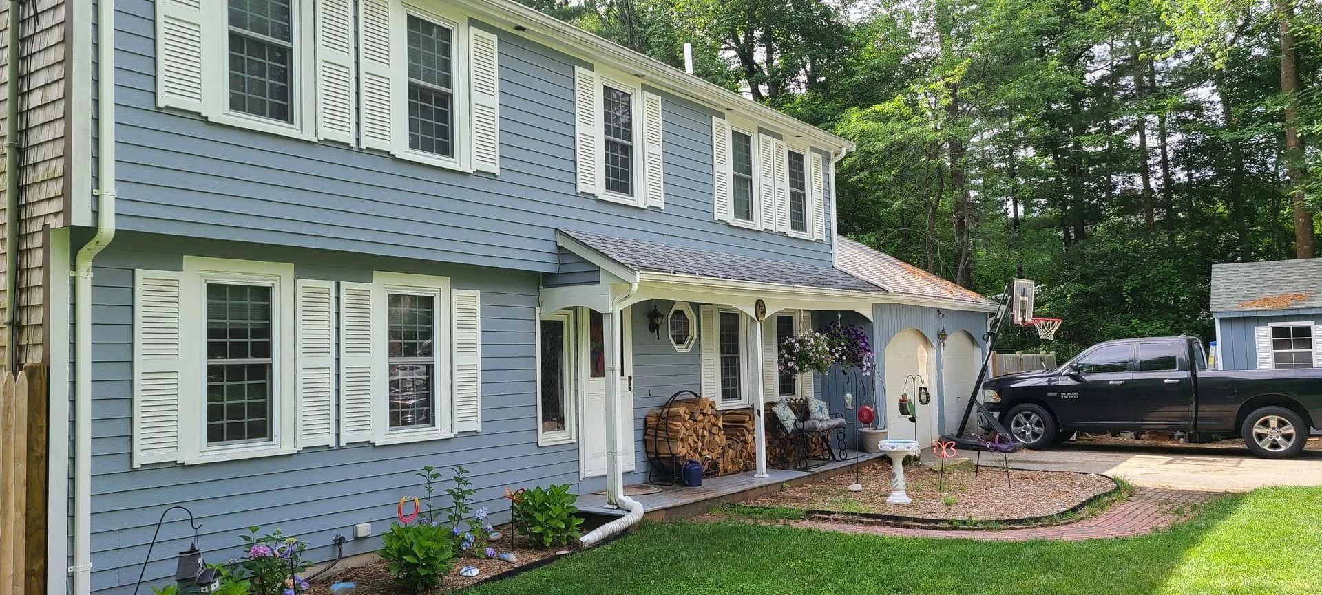 Blue house with white shutters, porch, and black truck parked in driveway.