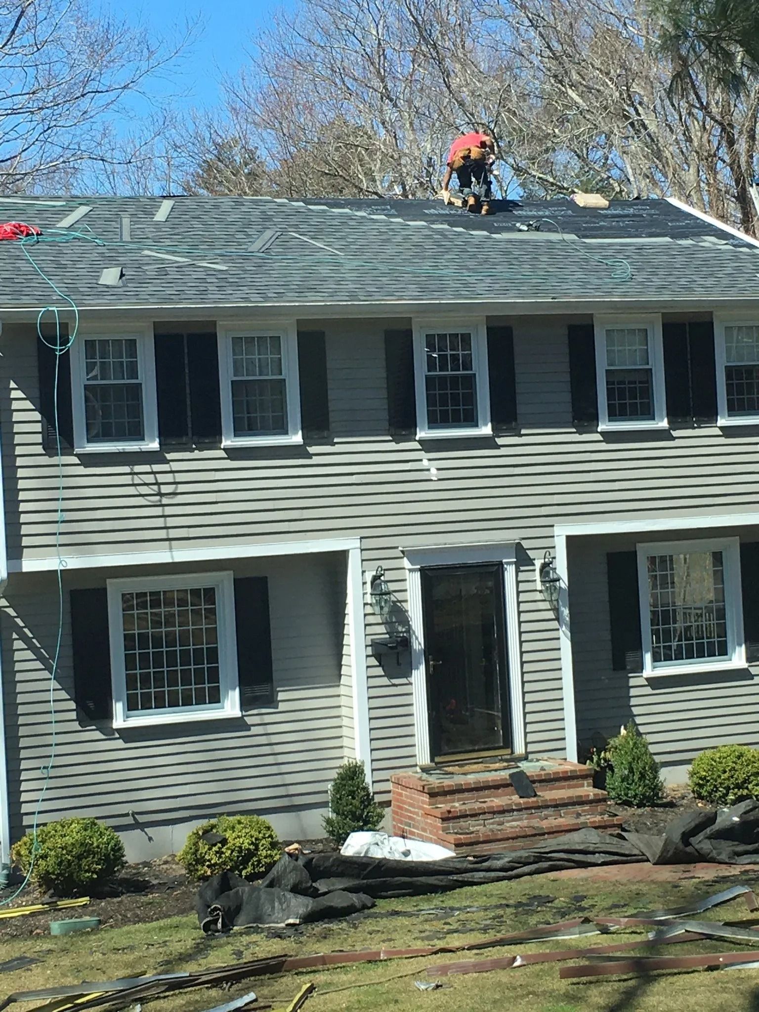 House with gray siding; a worker on the roof.