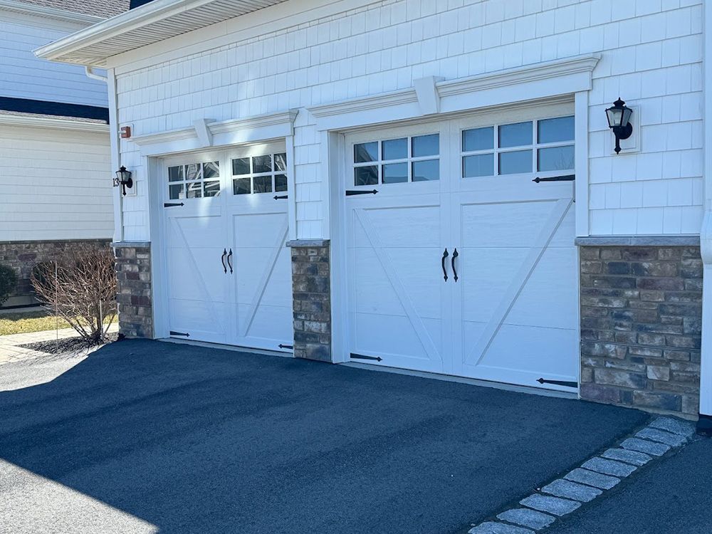 Two white garage doors with decorative trim and stone accents on a house, set in front of a driveway.
