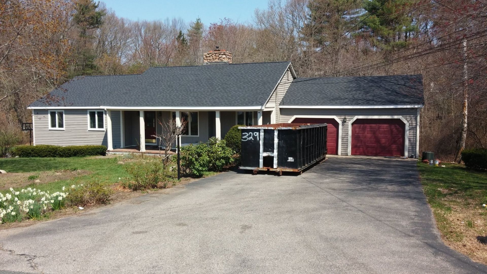 Ranch-style house with dark roof and red garage doors; dumpster in driveway.