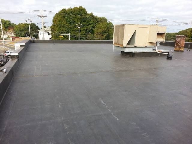 Flat black commercial roof with HVAC unit and brick chimney.