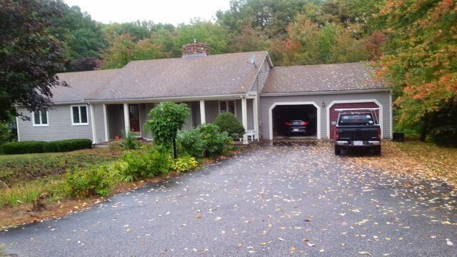 Gray house with attached two-car garage, black pickup truck in one bay, car in another, fall foliage.
