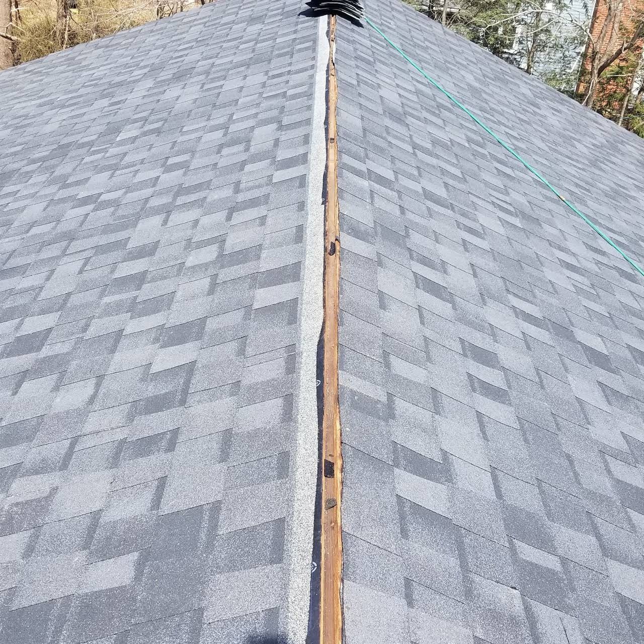 Close-up of a roof ridge. Gray asphalt shingles meet a wooden ridge beam.