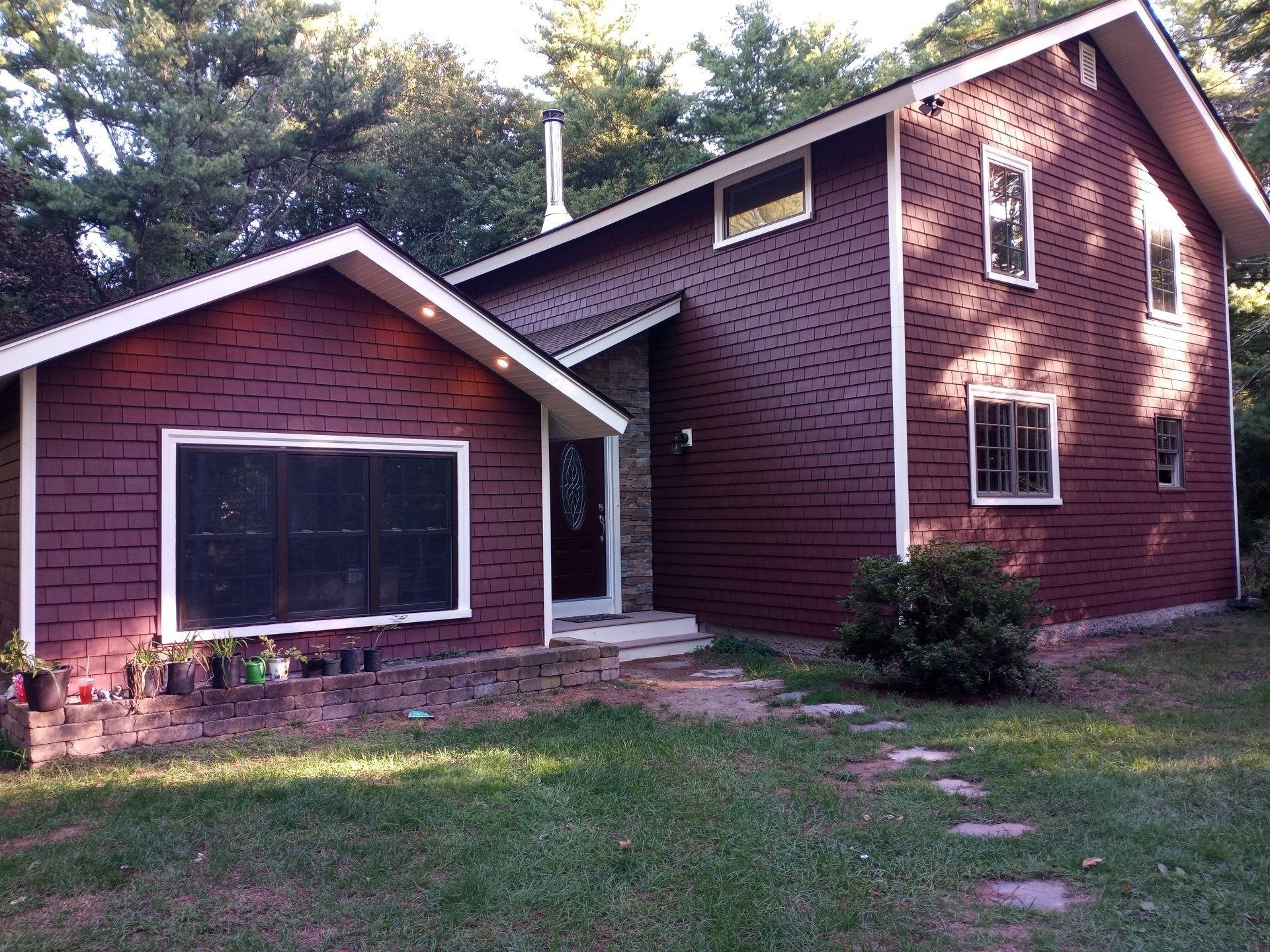 Two-story house with dark red siding, white trim, and a small porch. Path leads to the front door.