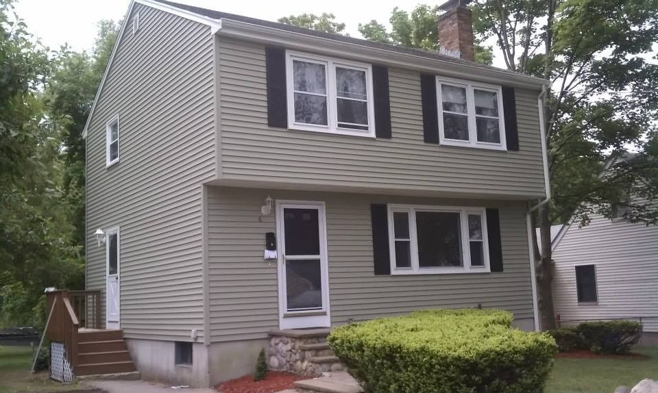 Two-story house with light green siding, black shutters, and a front door with a screen.
