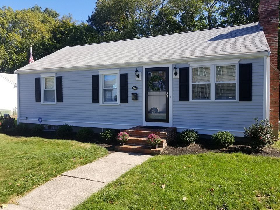 Light blue ranch-style house with black shutters, a sidewalk, and a small front garden with pink flowers.