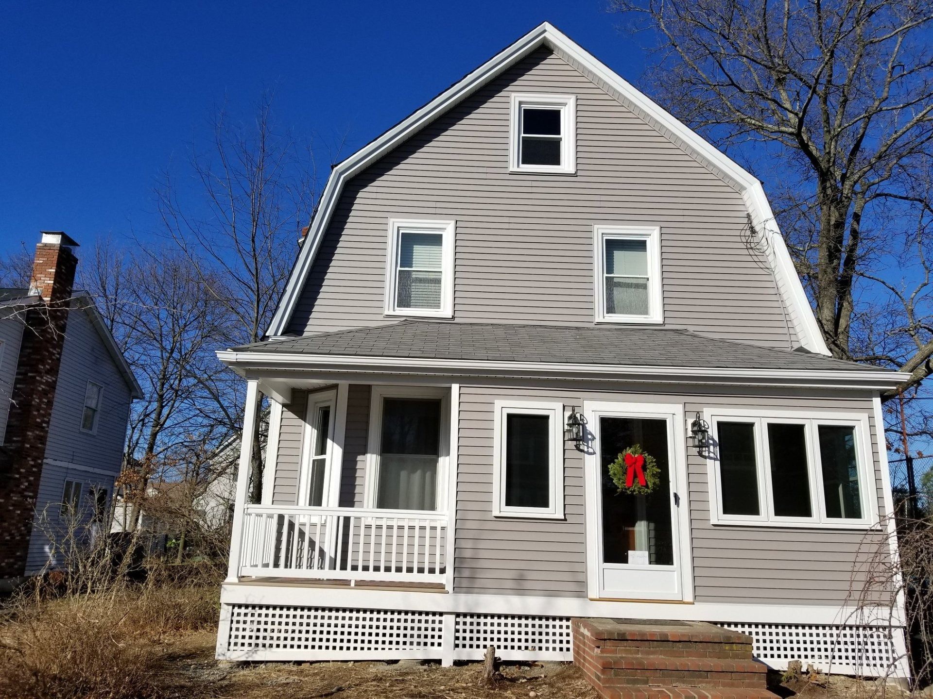 Gray house with Dutch gambrel roof and porch, on a sunny day.