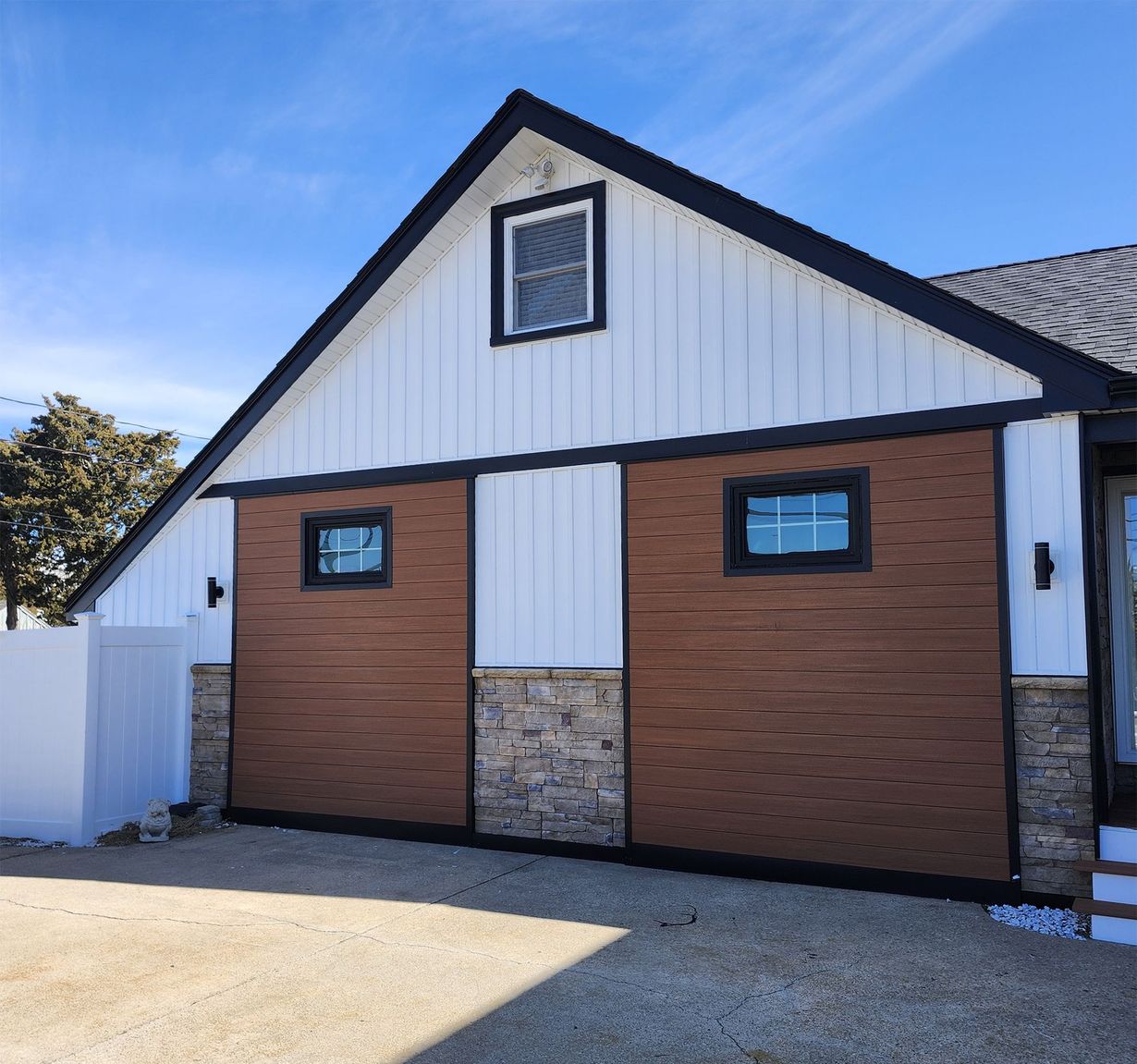 Two-story beige house with gray roof, stone accents, and two-car garage under an overcast sky.