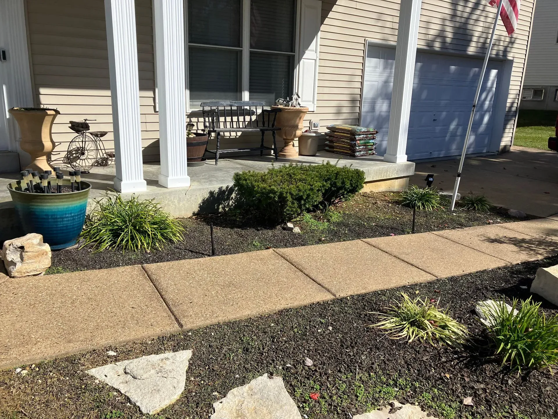 Brown stone walkway leading to a house with a porch, plants, and pots.