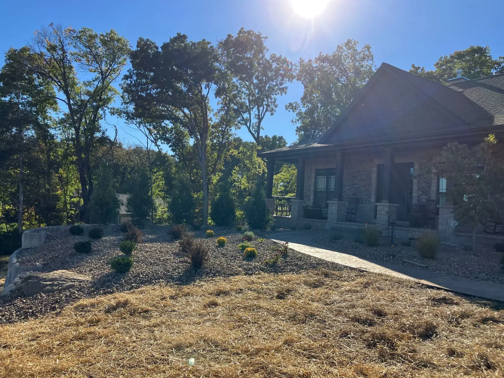 House with stone facade, porch, and a walkway, trees in the background, sunny day.