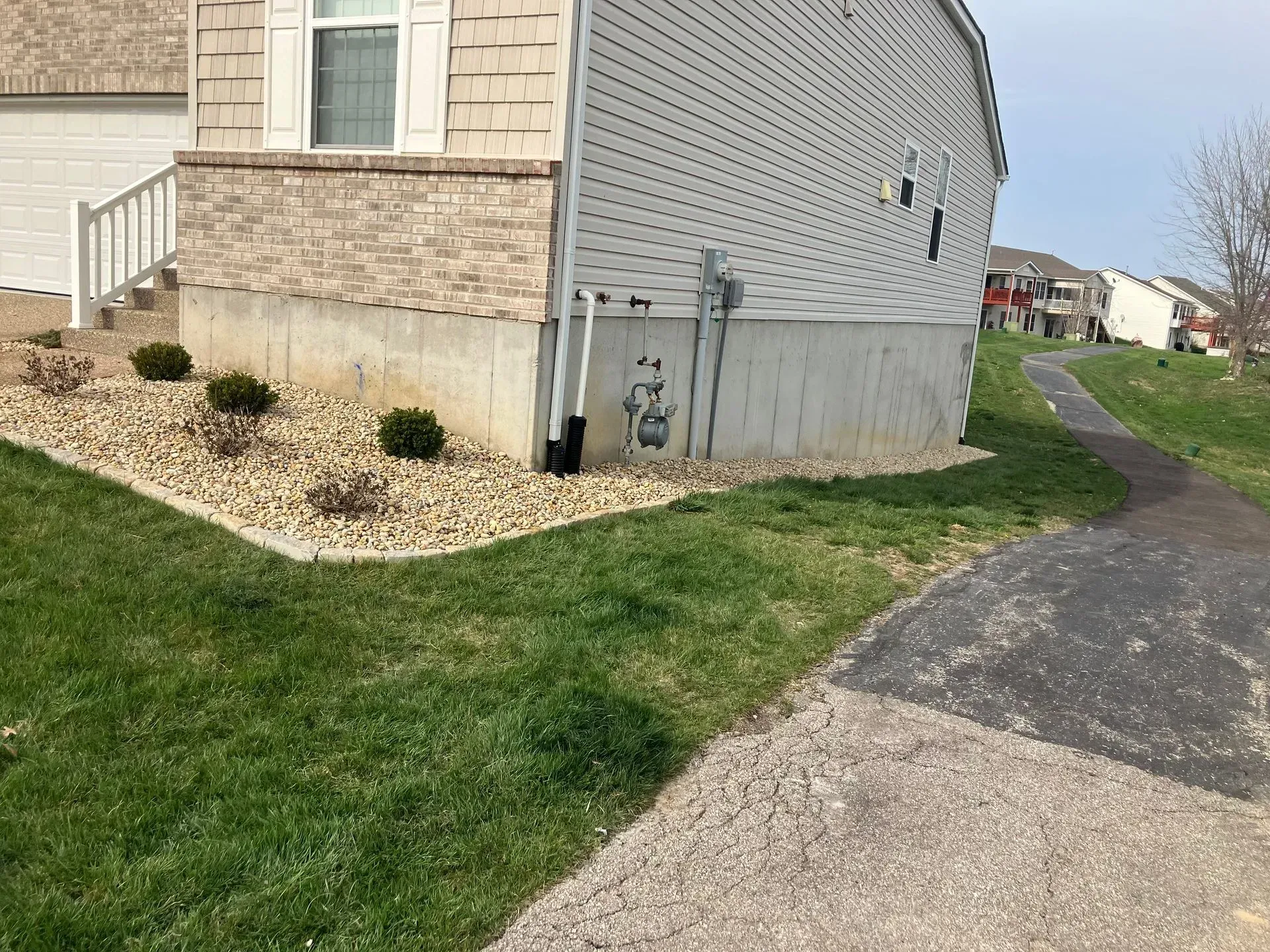 Corner of a house with landscaping, concrete foundation, and a pathway.