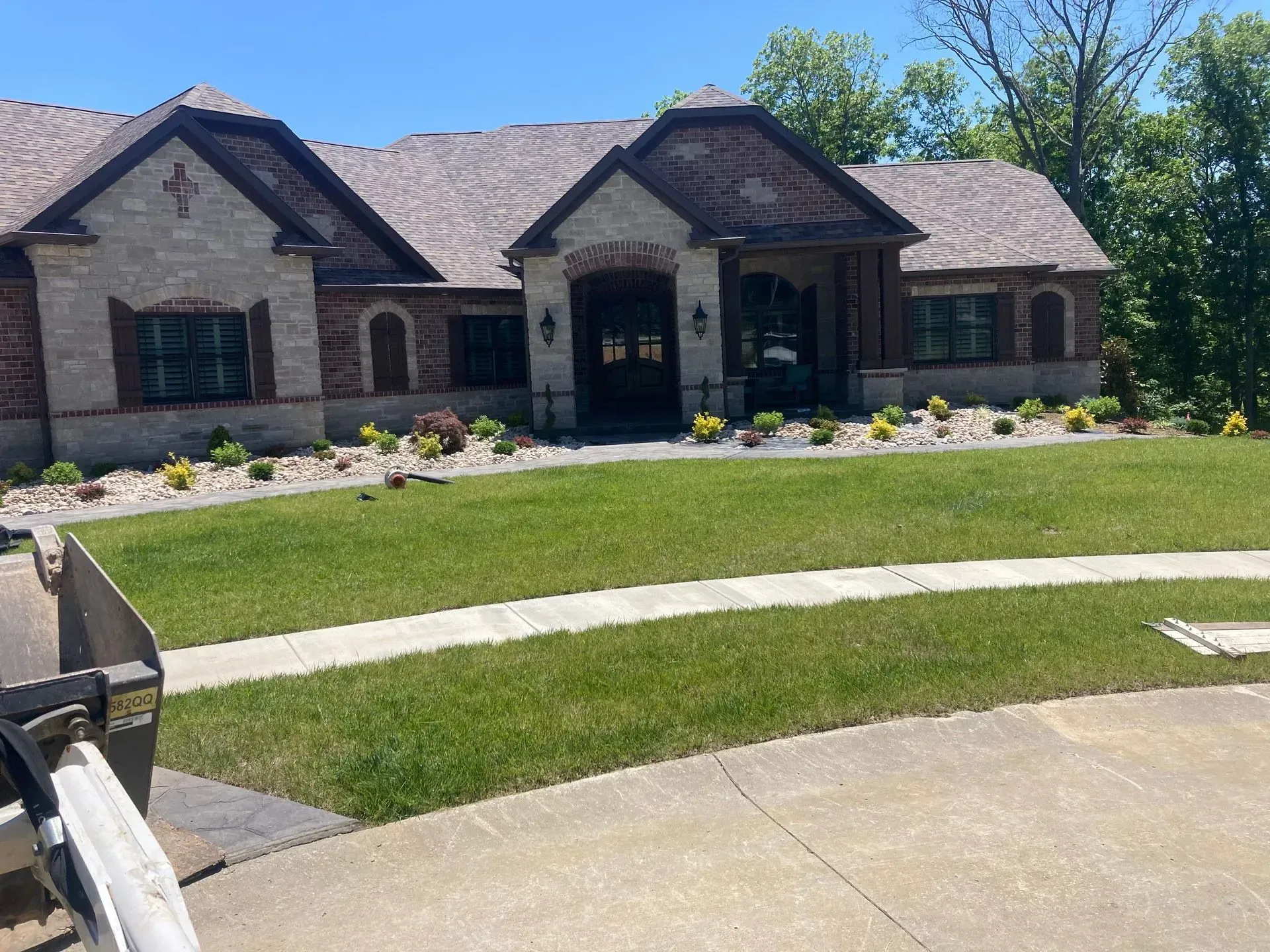 A brick and stone house with a well-manicured lawn and flower beds under a bright blue sky.