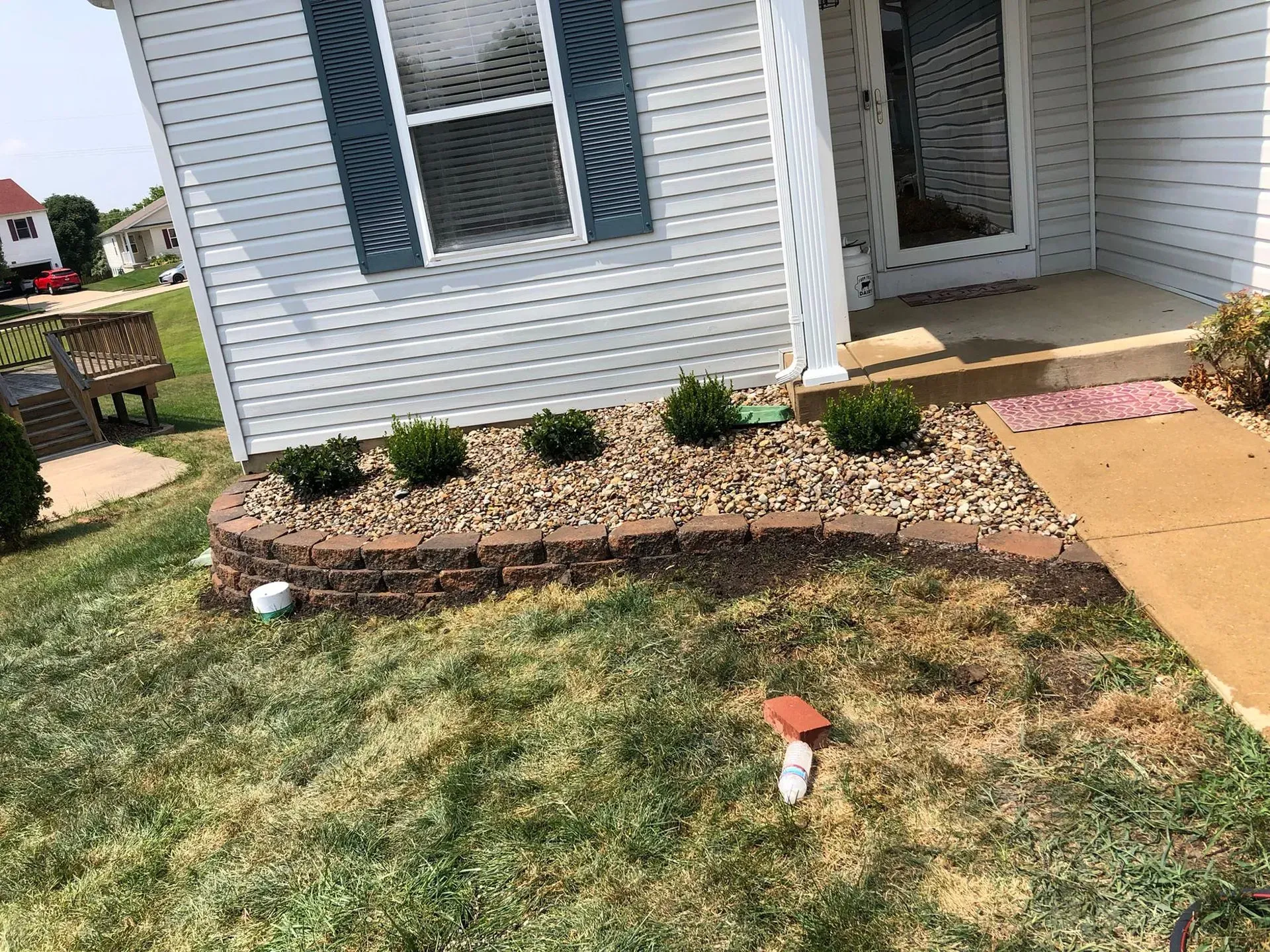 Front yard with a brick-lined flower bed, small green shrubs, and a concrete pathway leading to a front door.