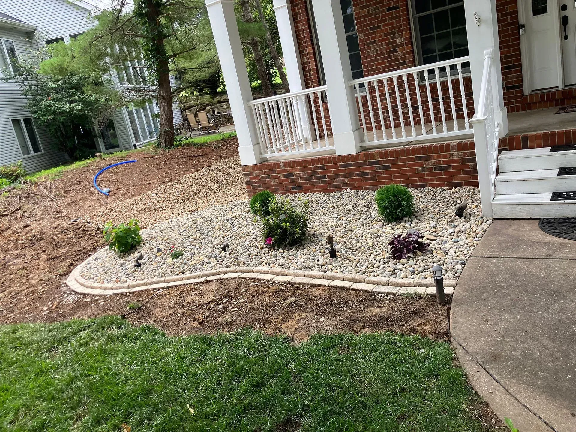 A house front yard with a landscaped bed of rocks, plants, and a curb edging.