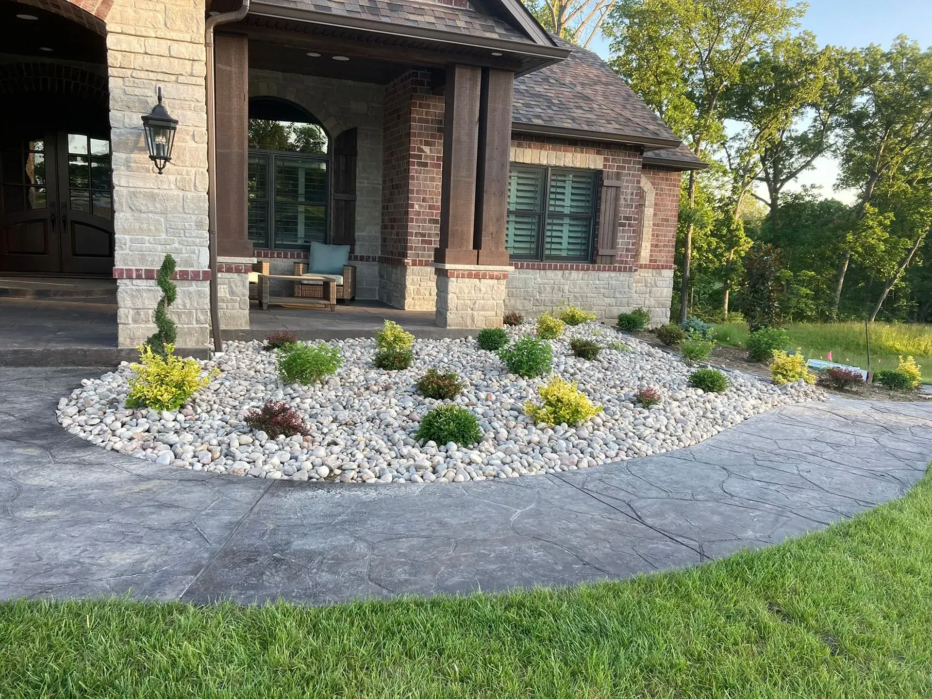 Landscaped yard with gray stone, green grass, and low-lying shrubs in front of a house.