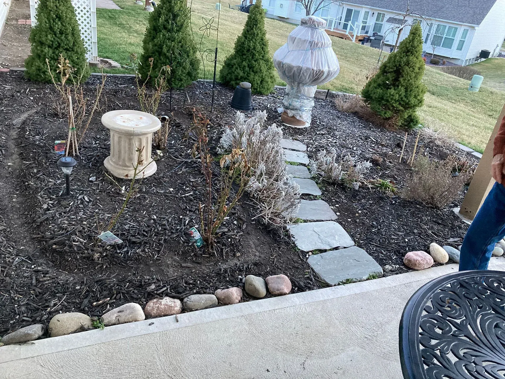 Flower bed with stone path, ornamental statues, and trimmed evergreen shrubs.
