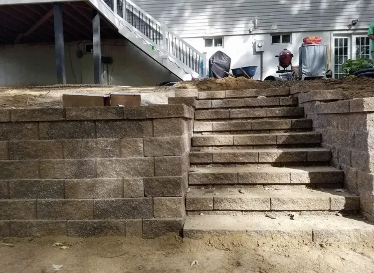 Stone retaining wall with built-in steps leading up to a house with a deck.