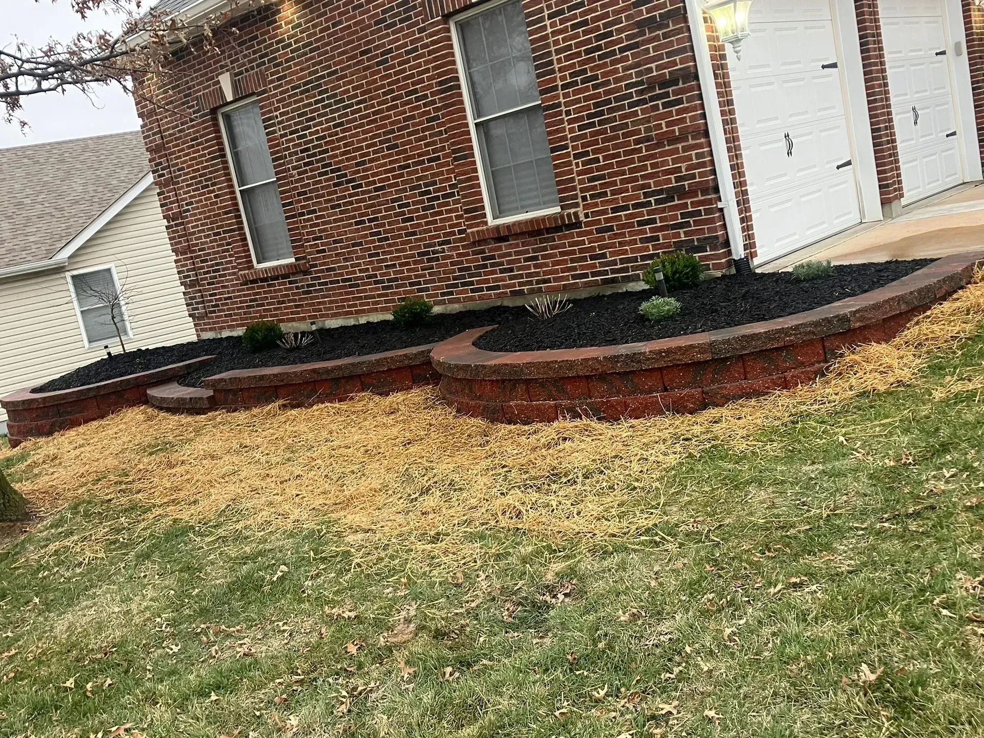 Brick house with curved, raised garden beds filled with dark mulch.