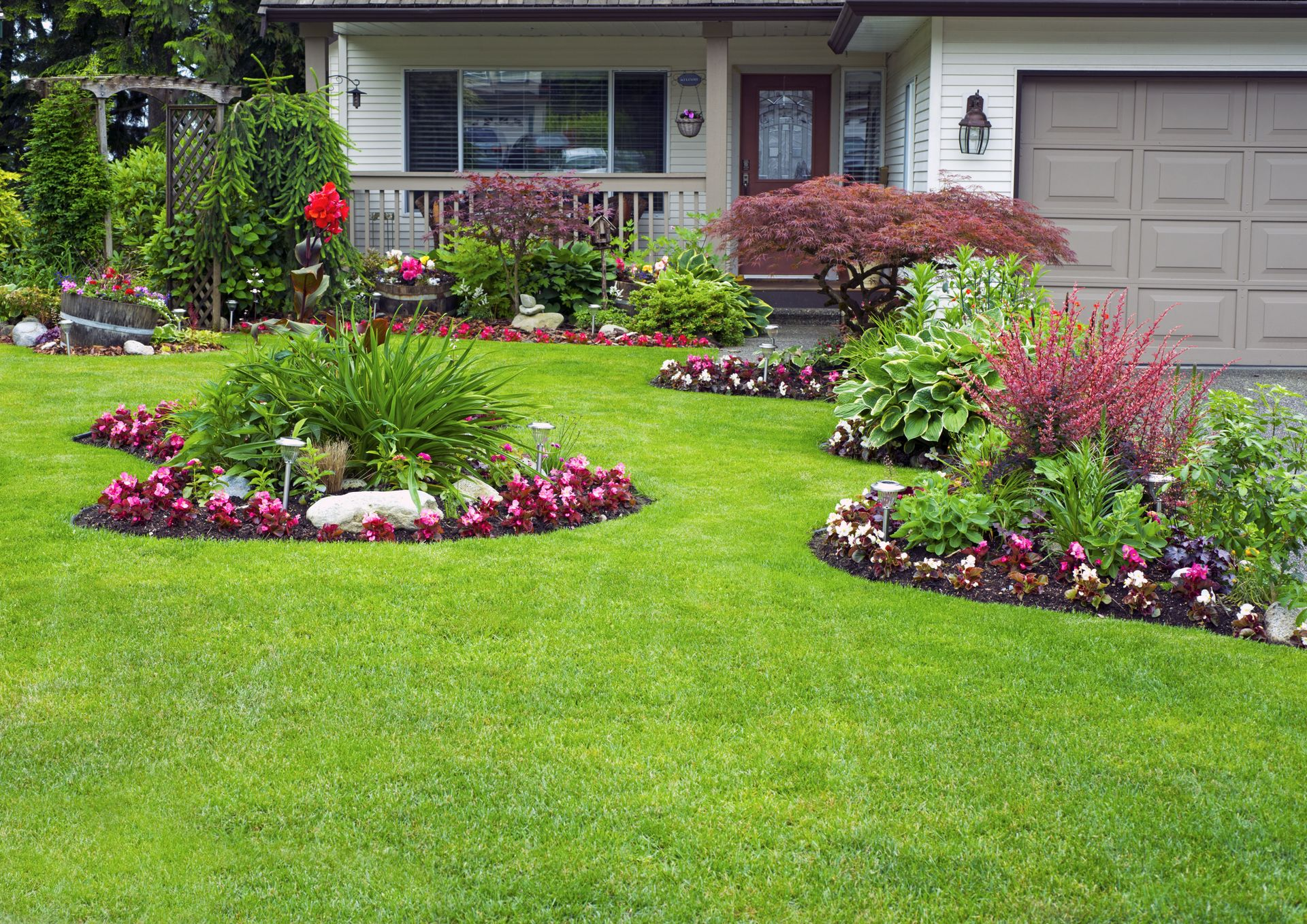 Lush green lawn with colorful flowerbeds in front of a house with a beige garage door.