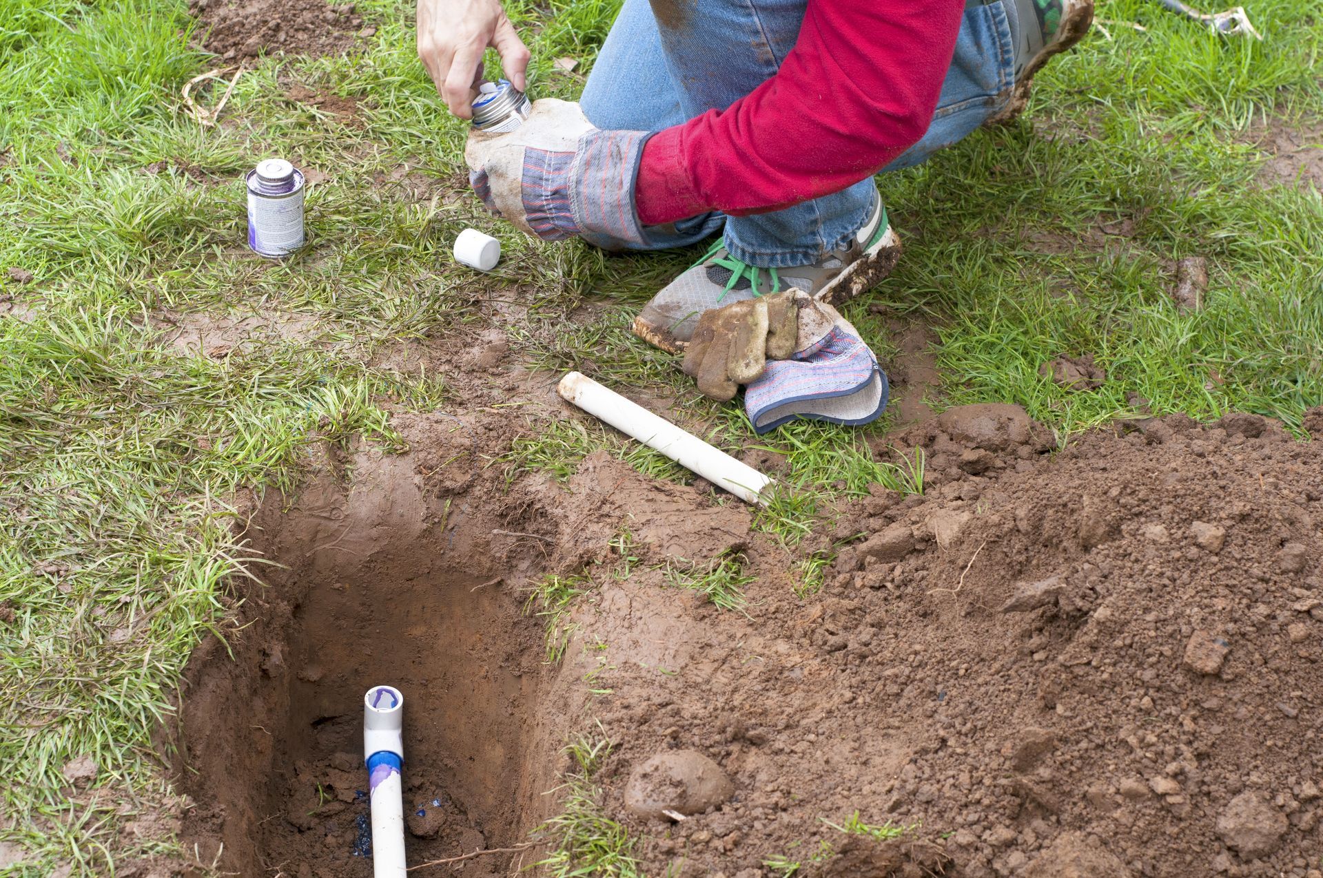 Person installing an underground sprinkler system component in a grassy area, using a cutter.