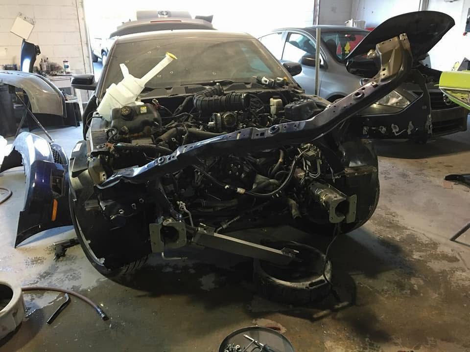 Severely damaged black car in an auto repair shop with its front end torn apart