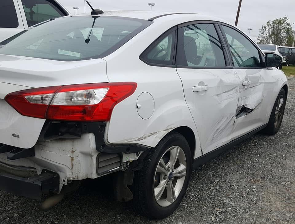 White sedan with rear-left damage and a dented rear door in a gravel lot