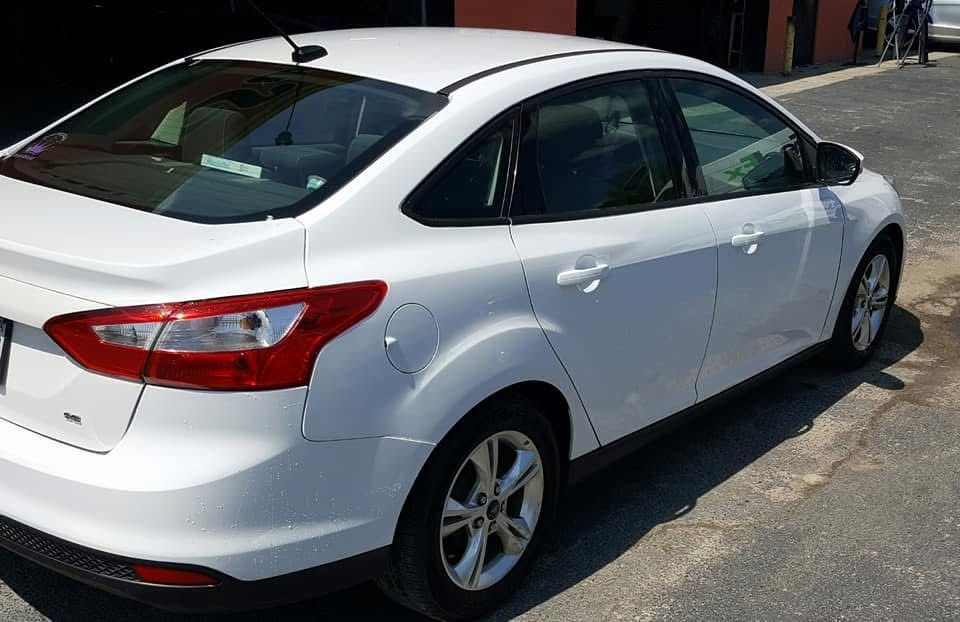 White sedan parked outdoors in a sunlit lot, rear three-quarter view.