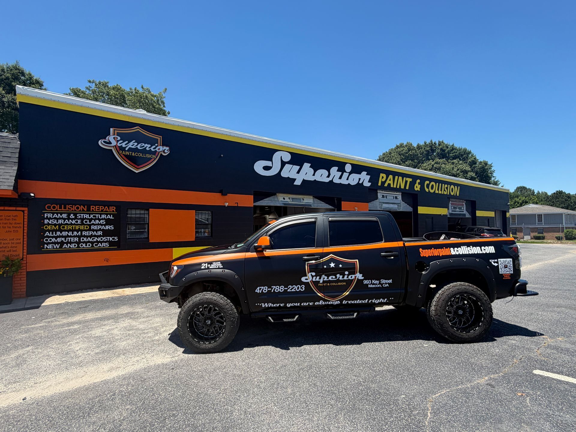 Black pickup truck parked outside a paint and body shop with a blue and orange storefront