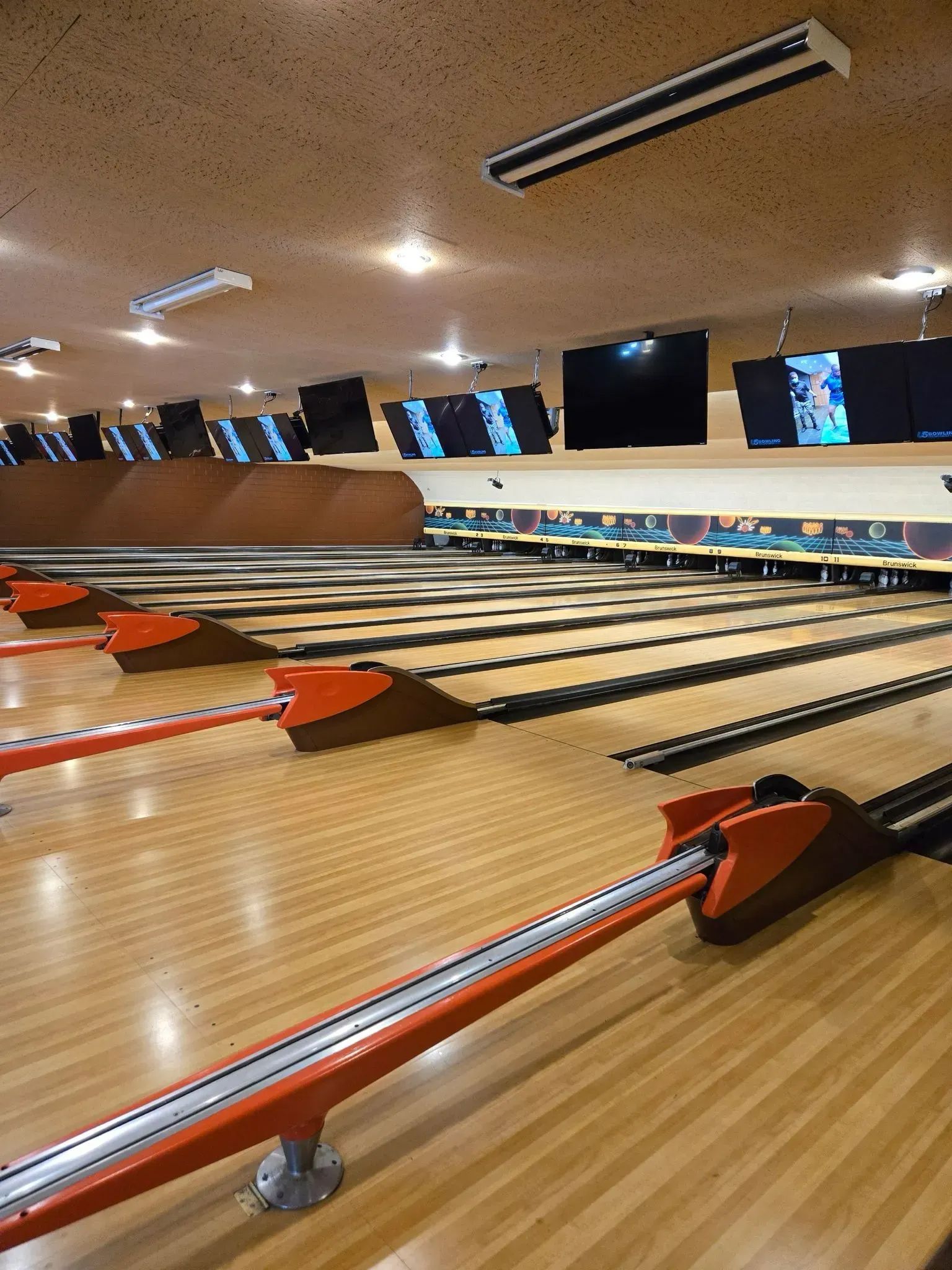 Bowling alley with wooden lanes, red ball returns, and overhead monitors in a brightly lit interior