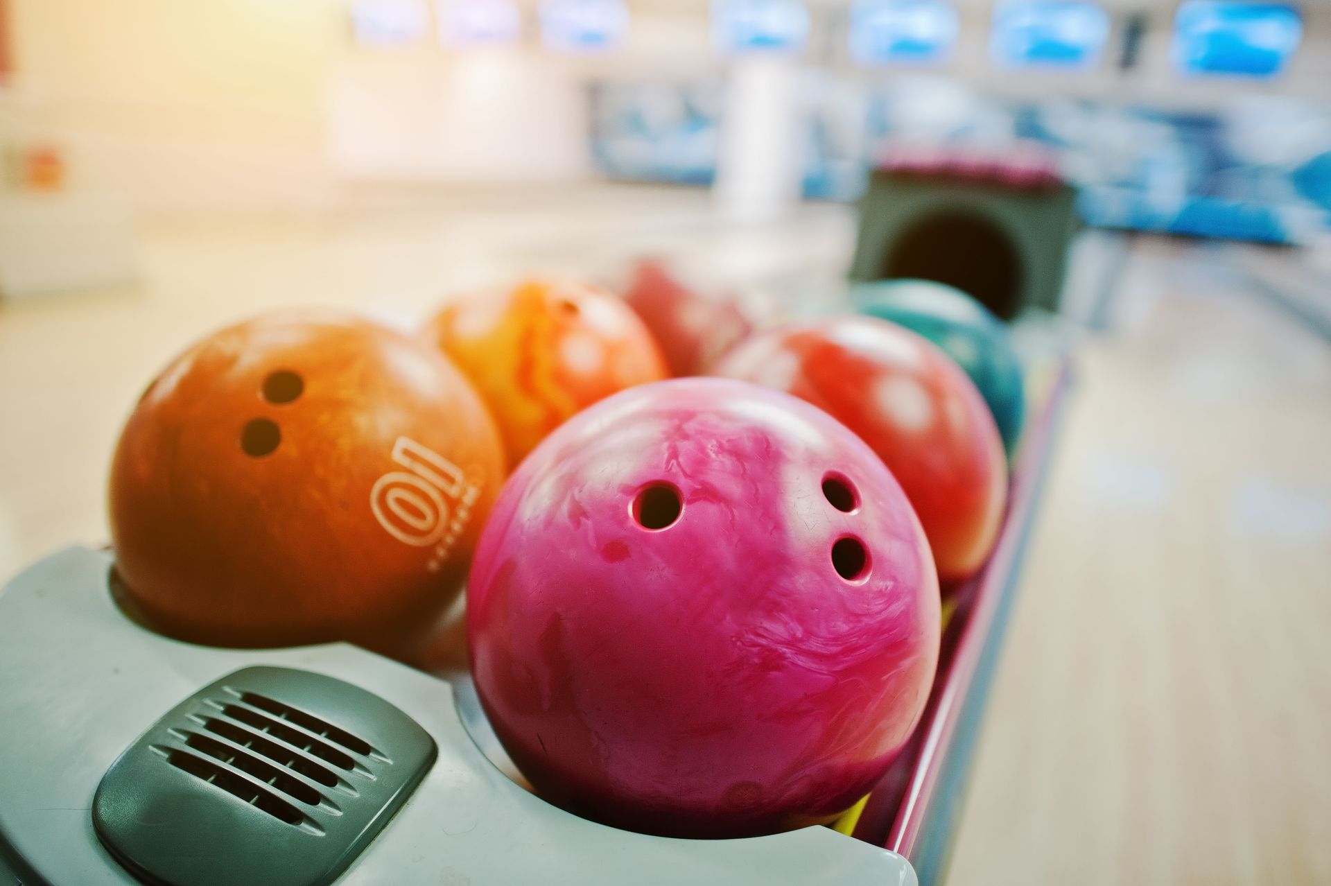 Colorful bowling balls lined up on a lane, with a pink ball in the foreground